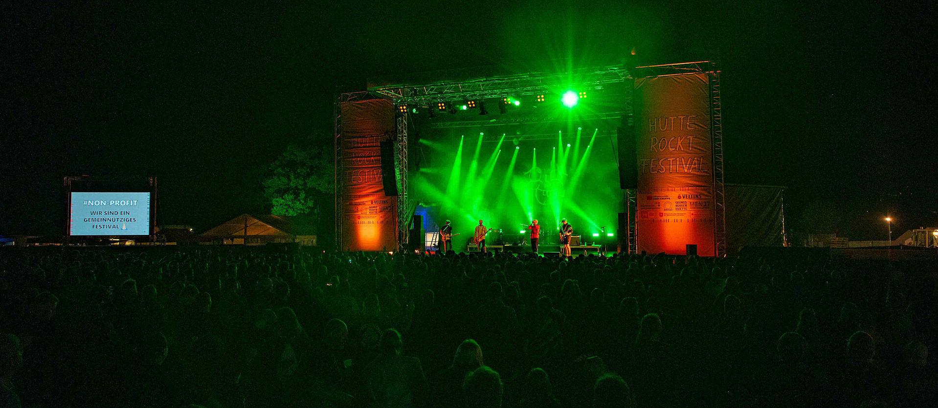 Die Hauptbühne des Hütte Rockt Festivals in dunkler Abendstimmung mit Beleuchtung und Menschenmenge