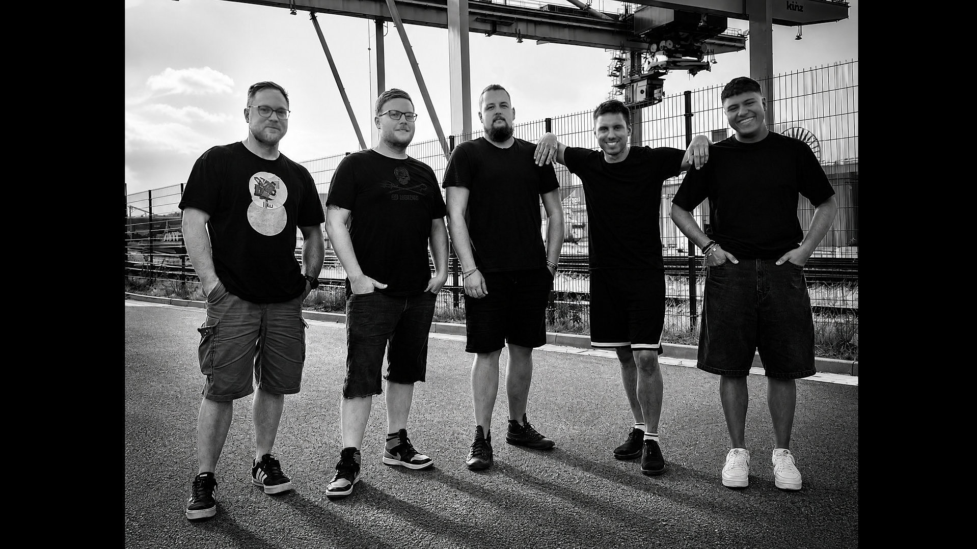 Die Mitglieder der Band in schwarz und weiß stehen vor Stahlträgern